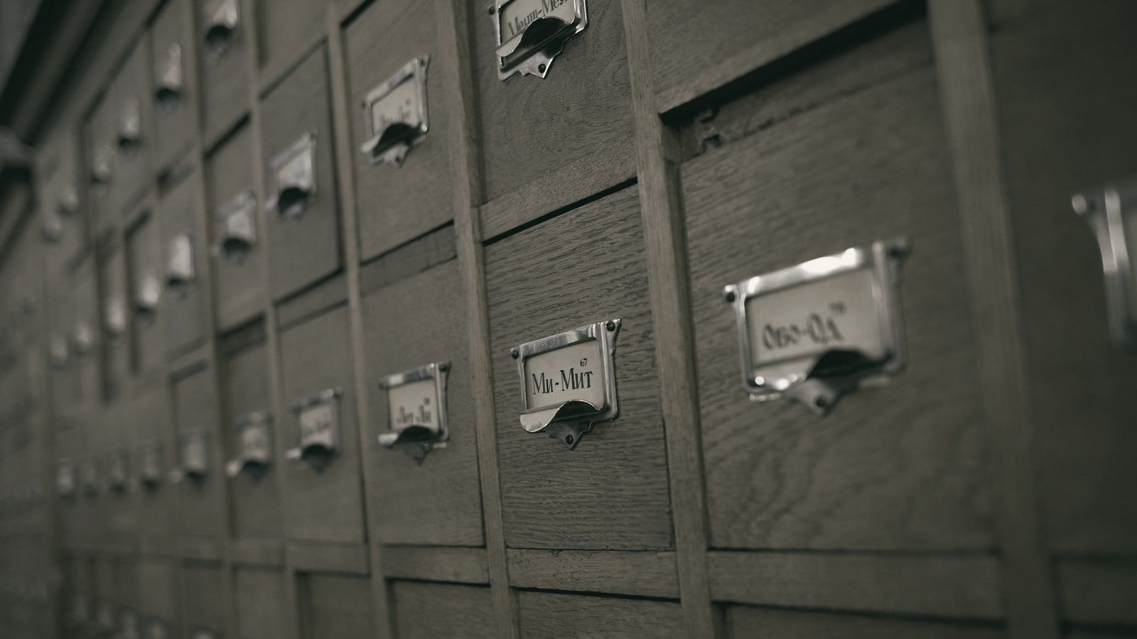 Fila de cajones de un fichero de biblioteca, de madera, con etiquetas metálicas que se pierden en perspectiva.