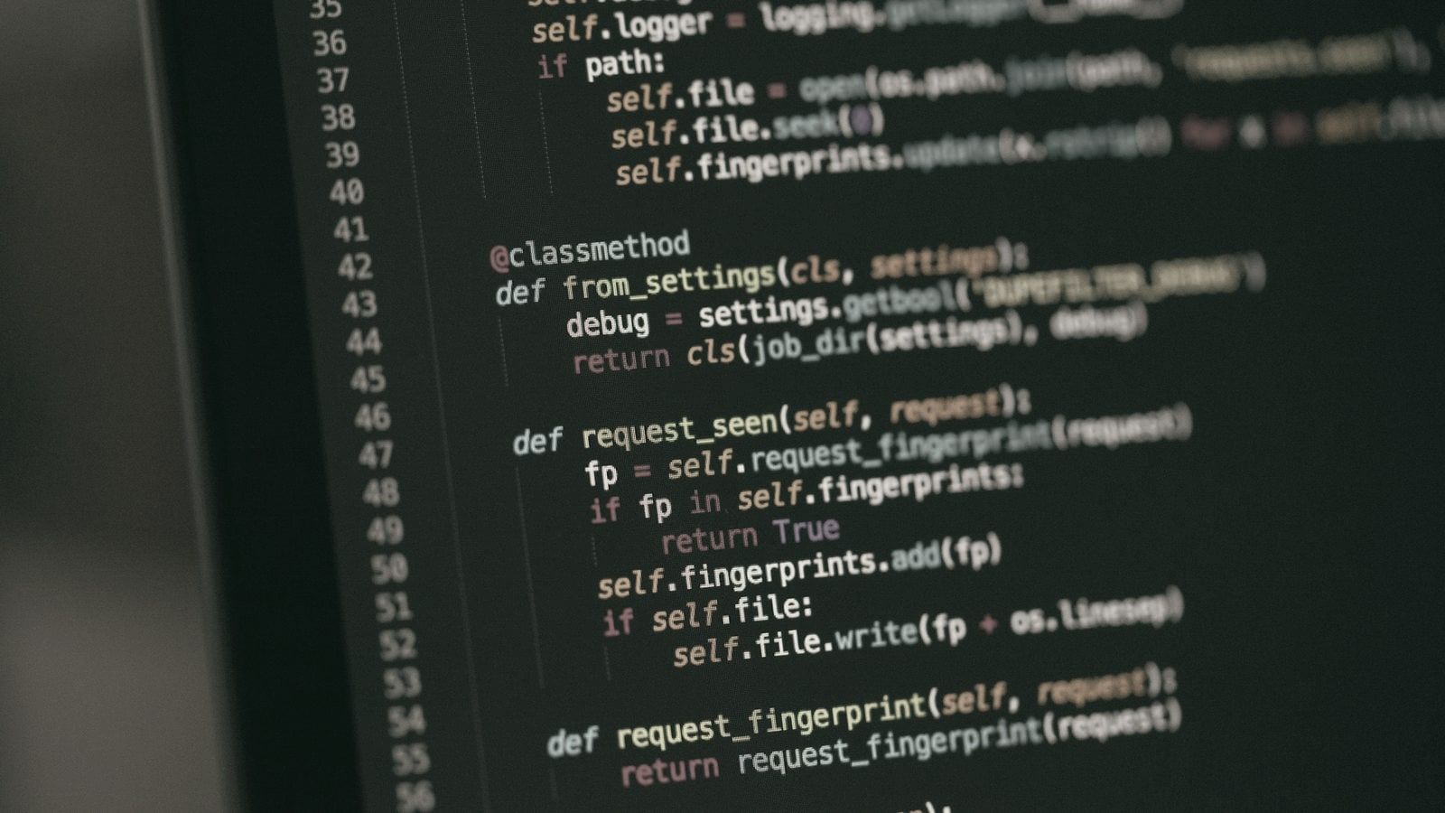 Screen in dim light seen at an angle, with colorful Python code on a black background that blurs toward the edges.