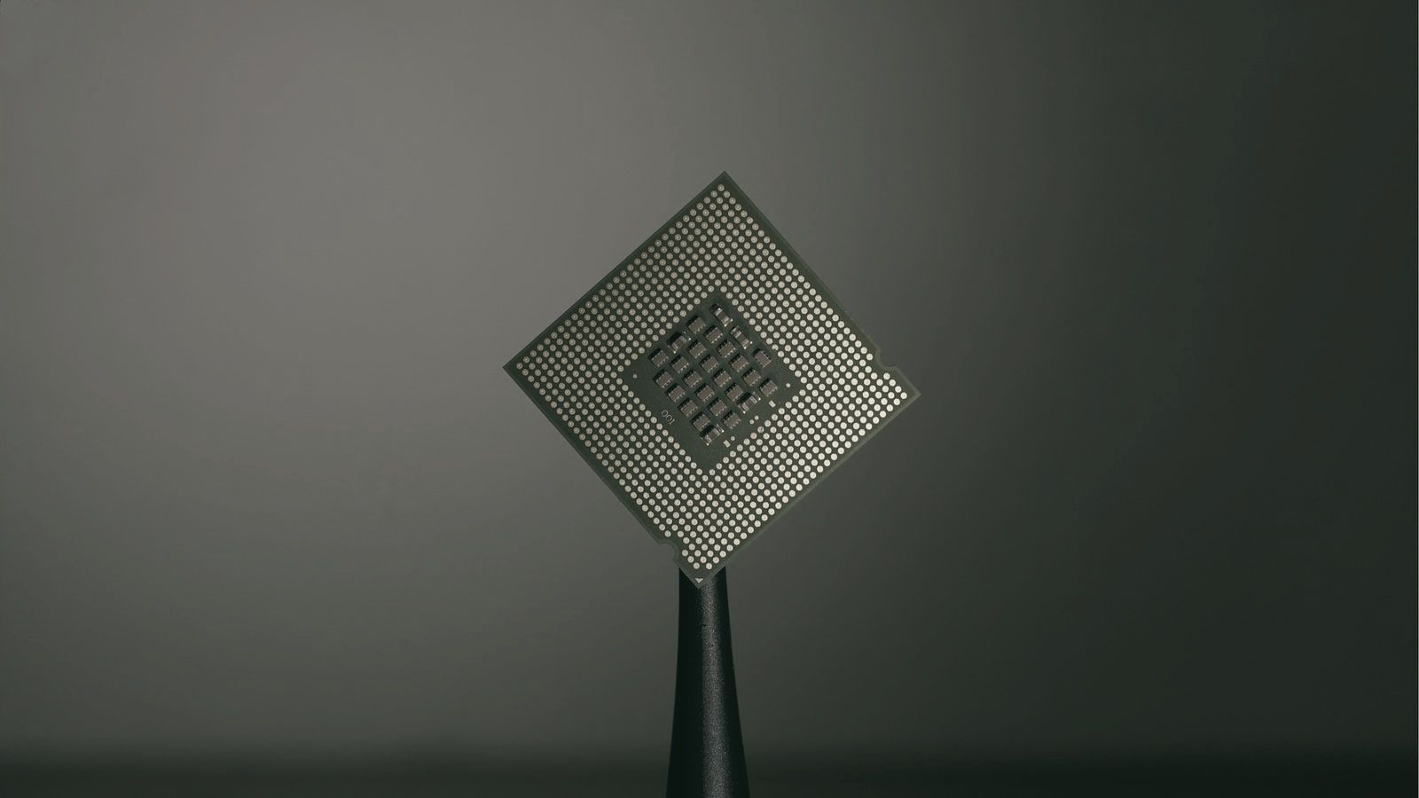 A processor seen from below, held up with tweezers, its gold contacts against a dark, blurred background.
